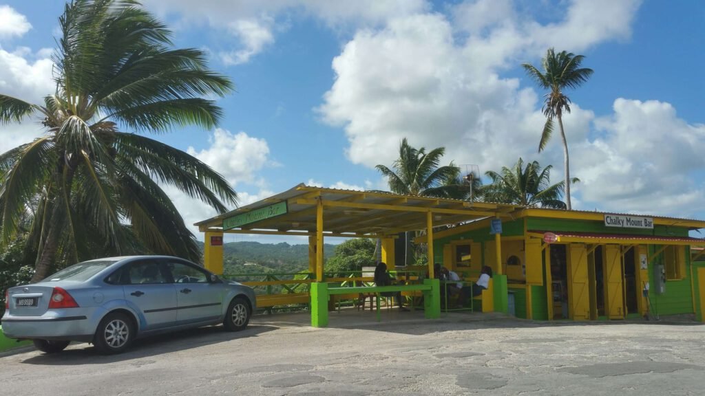 Colorful Chalky Mount Bar rum shop in Barbados with bright yellow and green exterior, flanked by lush palm trees under a blue sky