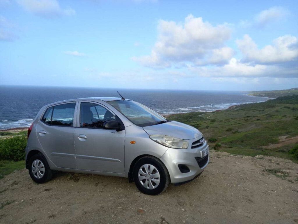 Silver economy car parked on a cliff with a panoramic view of the East Coast of Barbados in the background