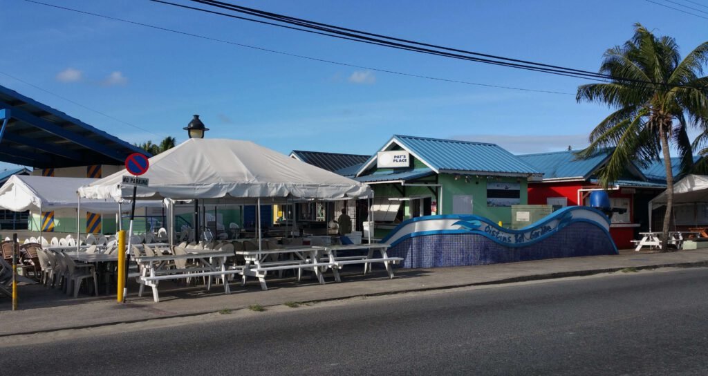 Outdoor dining area of Oistins Fish Fry Market in Barbados with white tents and casual seating under a clear blue sky