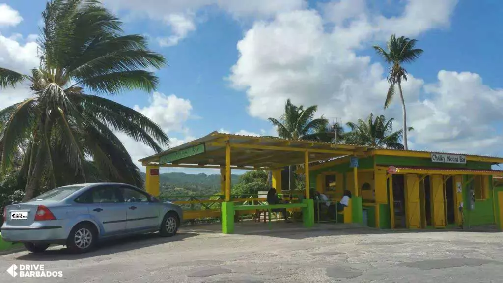 Colorful Chalky Mount Bar rum shop in Barbados with bright yellow and green exterior, flanked by lush palm trees under a blue sky