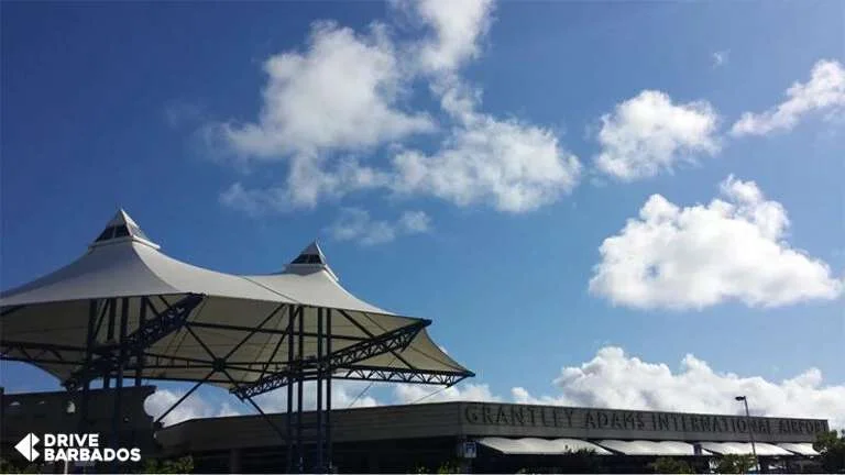 Entrance of Grantley Adams International Airport in Barbados, with modern white tensile fabric structures against a bright blue sky with fluffy clouds