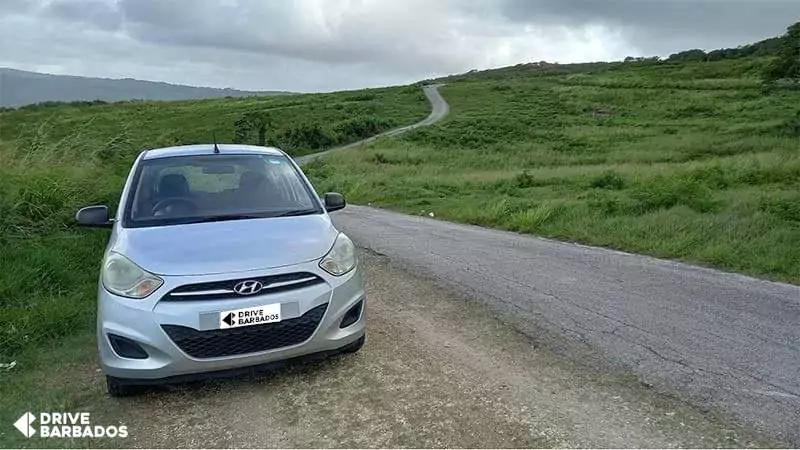 Drive Barbados rental vehicle parked on rural road with scenic green landscape