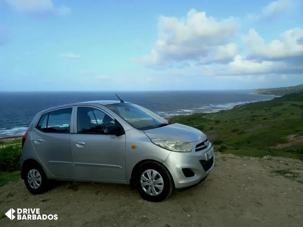 Drive Barbados rental car parked on a cliff overlooking the scenic east coast of Barbados.